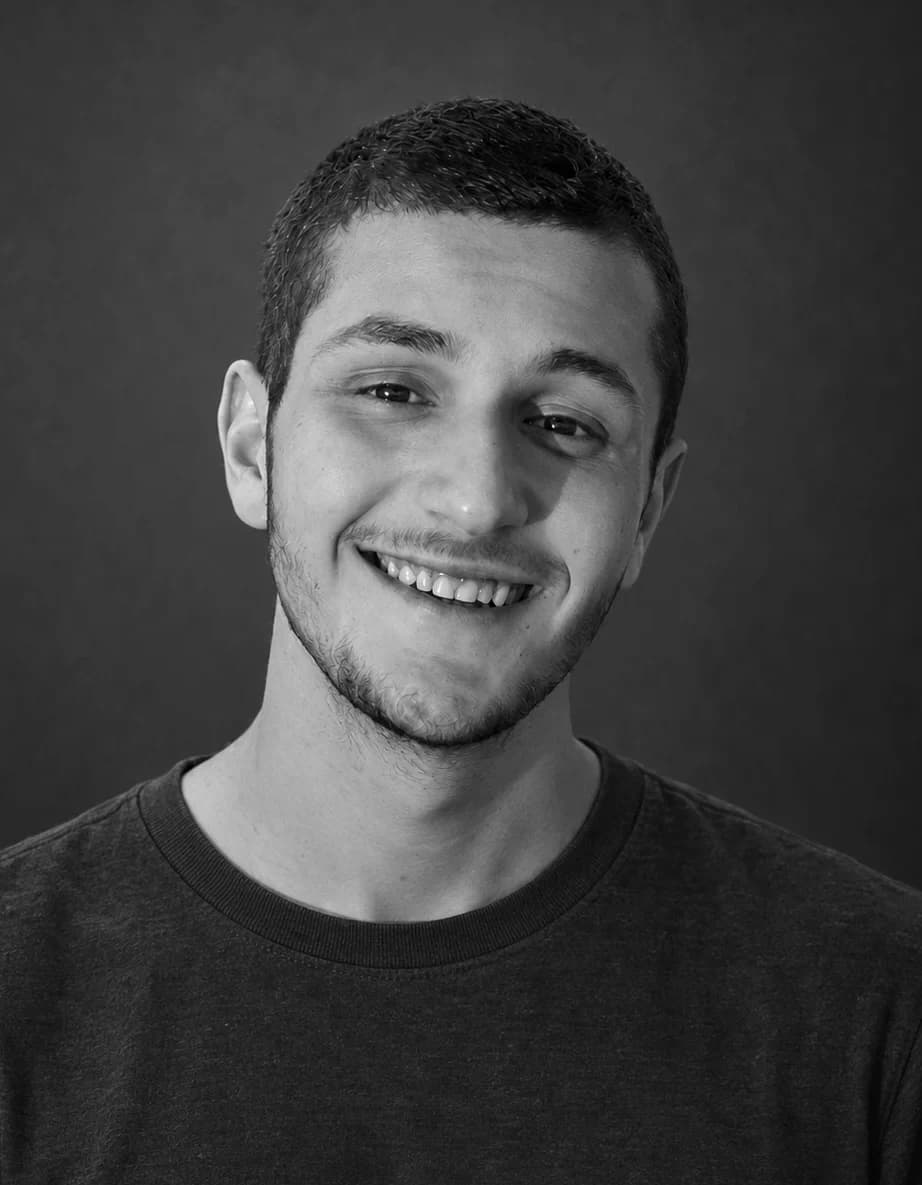 Jonathan Rashi, smiling, in a dark T-shirt against a gray wall