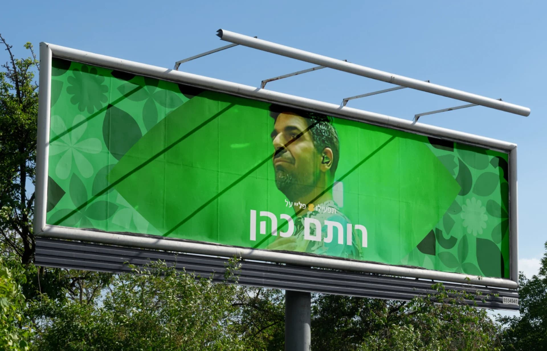 A green roadside billboard featuring Rotem Cohen, his name in Hebrew and shapes from the identity.