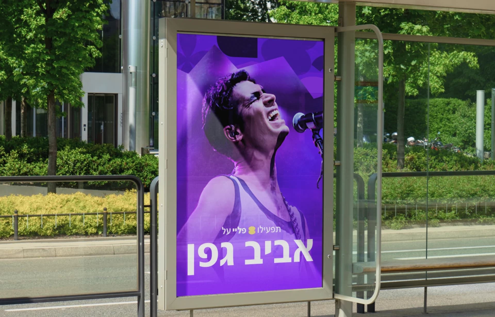 A purple bus-shelter poster featuring Aviv Geffen’s portrait and his name in large white Hebrew letters.